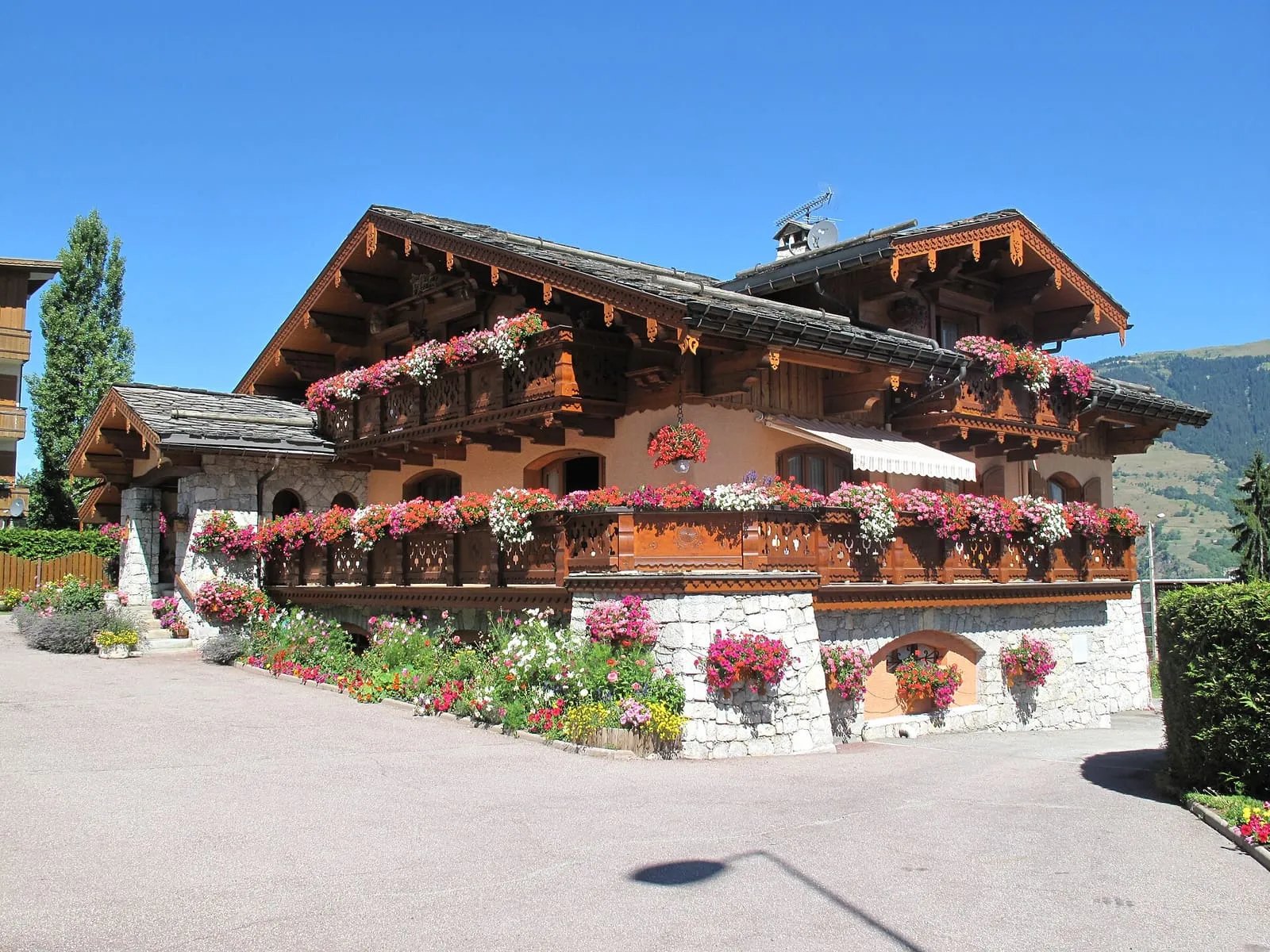 Grand chalet aux balcons couverts de géraniums, soubassement en pierre blanche